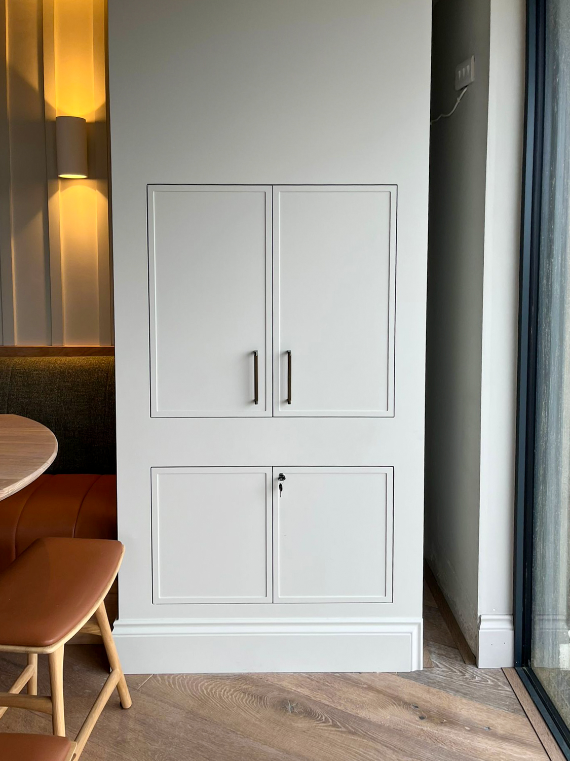White built-in cabinetry with two upper doors and two lower doors, next to a wooden bench and table.