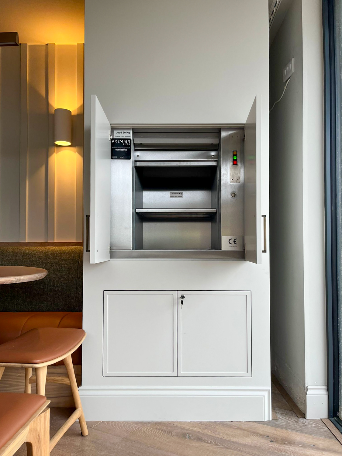 Built-in dumbwaiter lift with open white doors inside a modern dining area.