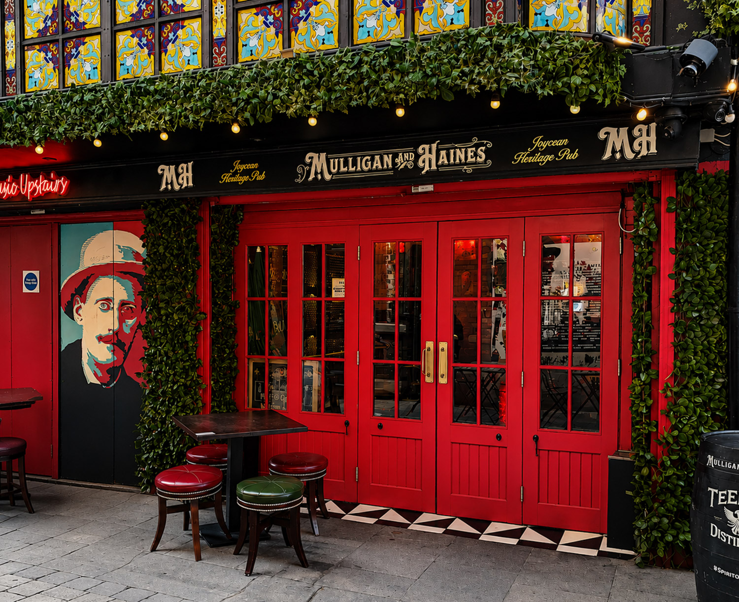 Entrance of Mulligan and Haines pub in Dublin with red doors, green vines, stained glass, seating, and a portrait mural.