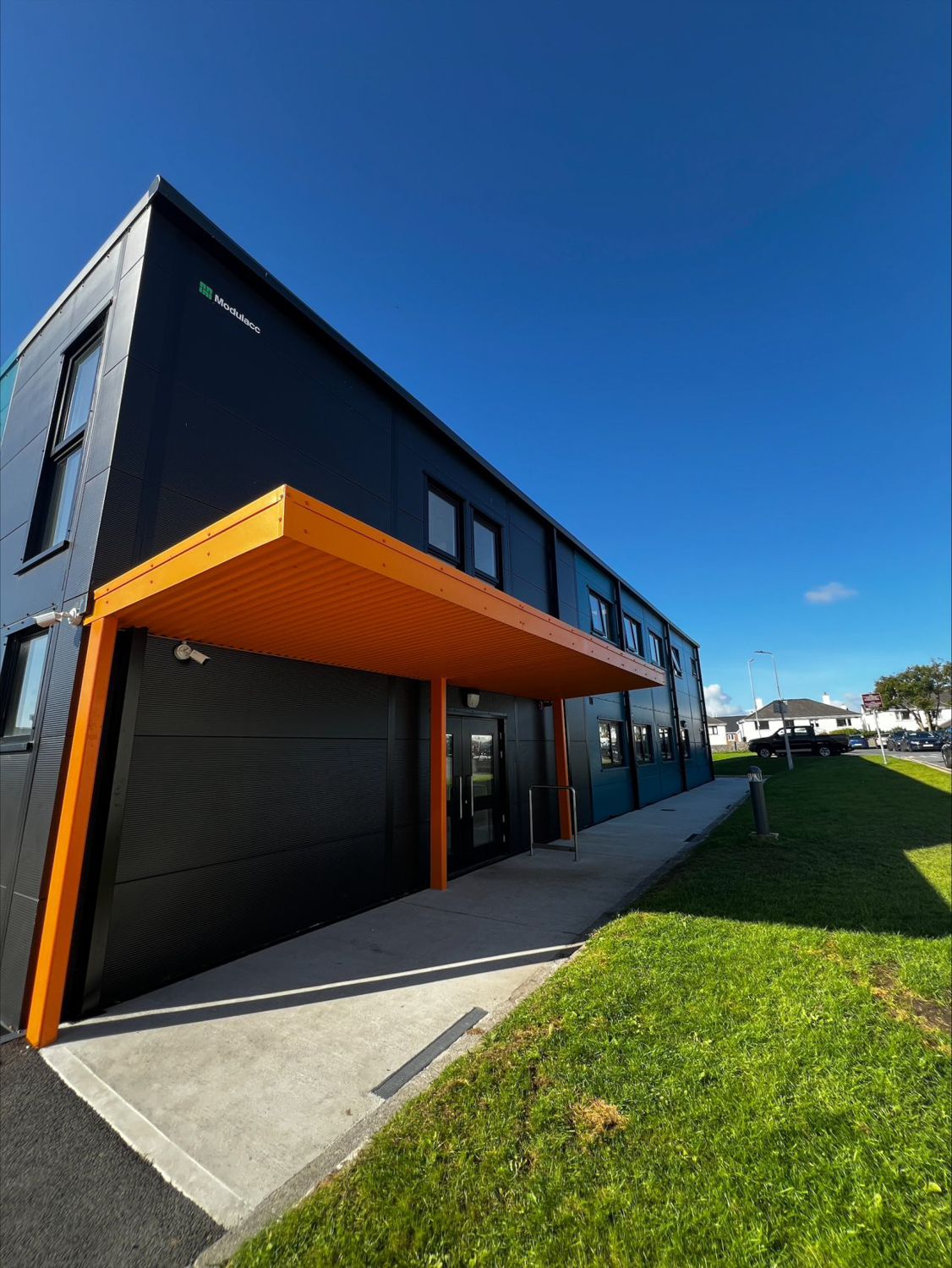 Modern black building with orange canopy over entrance and clear blue sky above.