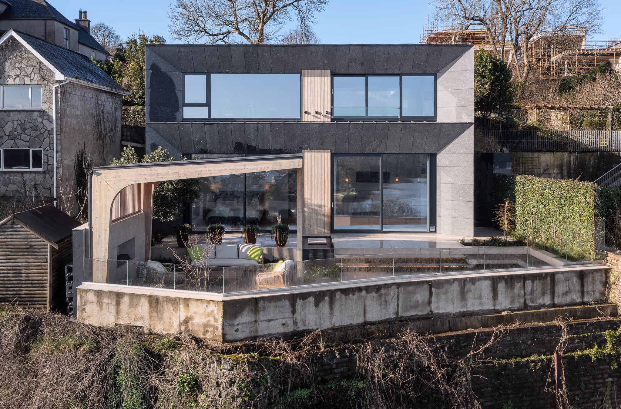 Modern two-story house in Kinsale with large glass windows and a wooden pergola over the patio area.