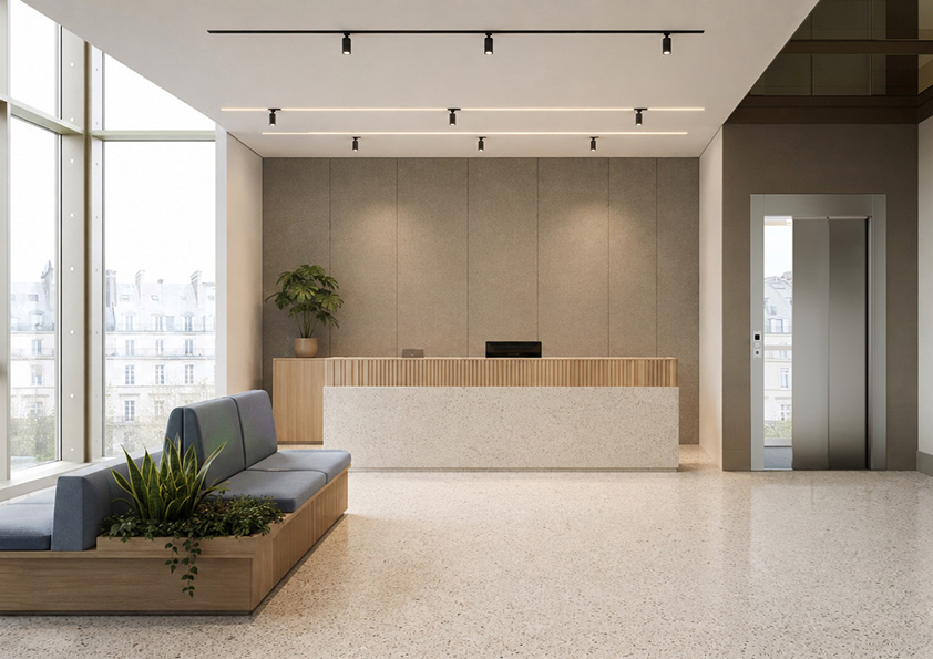 Modern lobby with a light terrazzo floor, a wooden reception desk against a beige wall, a potted plant on the desk, blue cushioned bench seating with built-in planters, large floor-to-ceiling windows on the left, and a closed public elevator with metallic doors on the right.