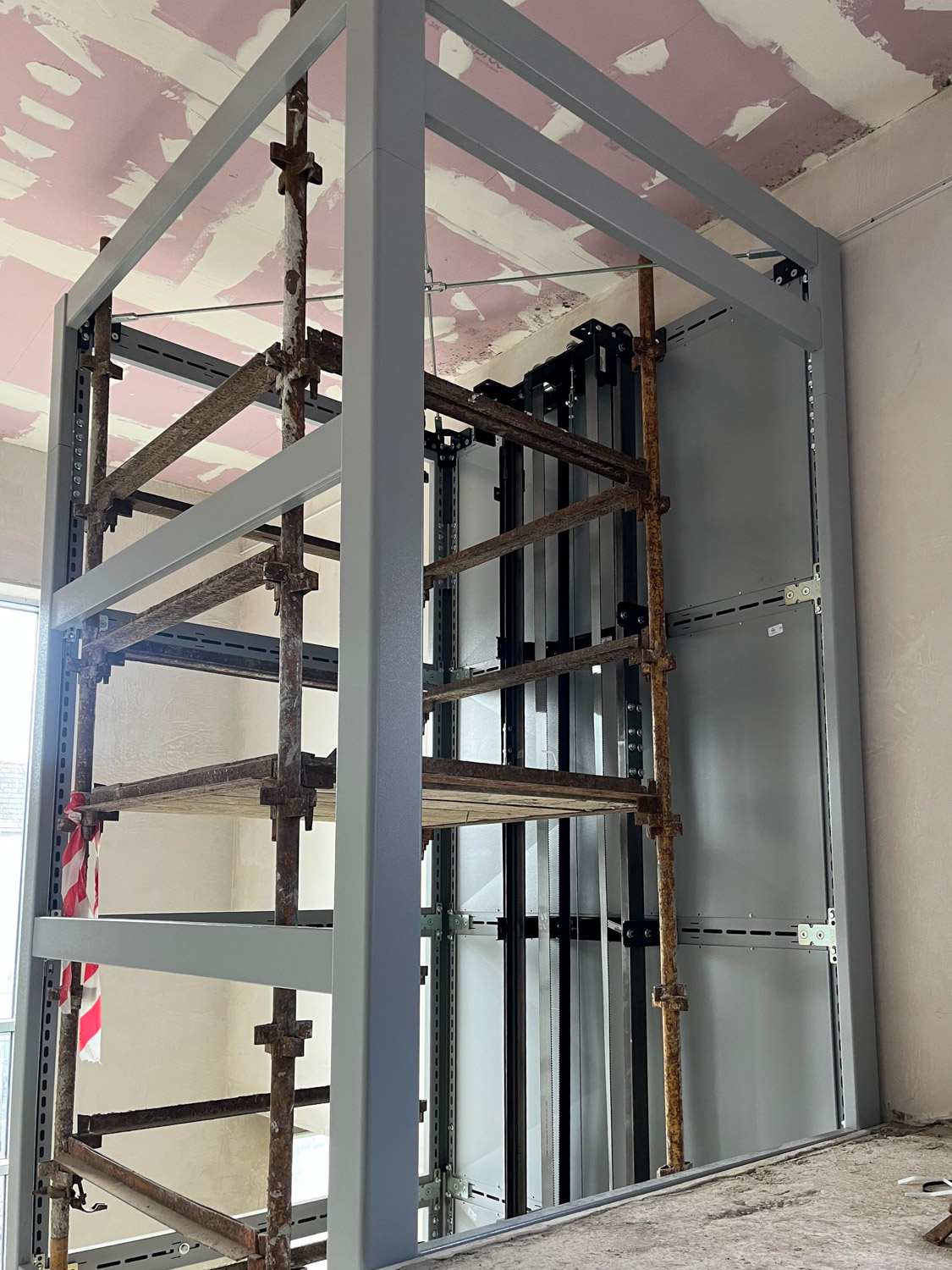Metal and wood scaffolding structure inside a building under construction, with gray painted metal beams and a partially finished ceiling.
