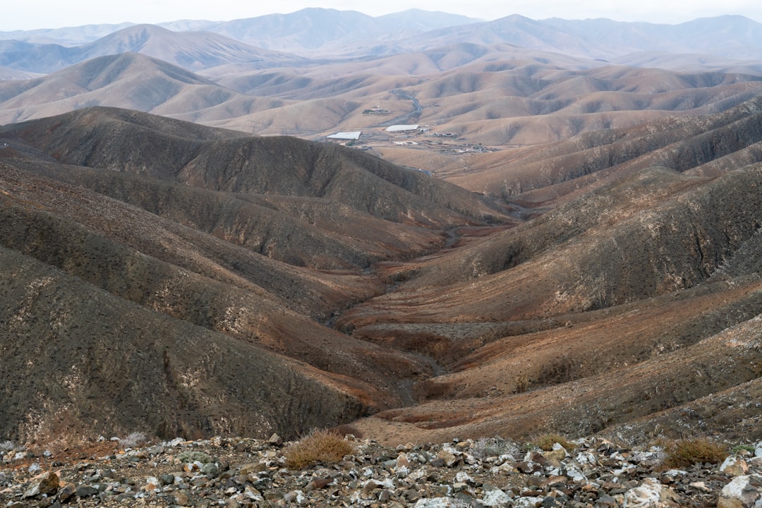 Arid mountain valley with dry brush and distant buildings