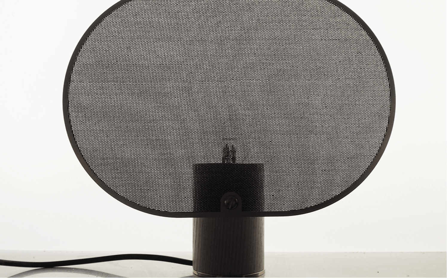 Black mesh pop filter on a stand in front of a microphone against a white background.