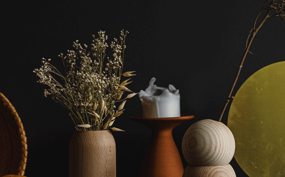 Wooden vase with dried flowers next to a clay candlestick with a partially melted white candle.