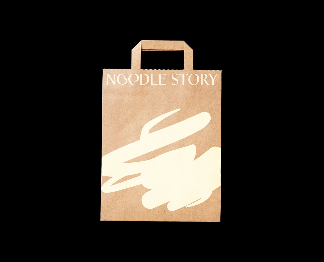 Kraft paper bag with handles and 'NOODLE STORY' text and abstract white design on front.