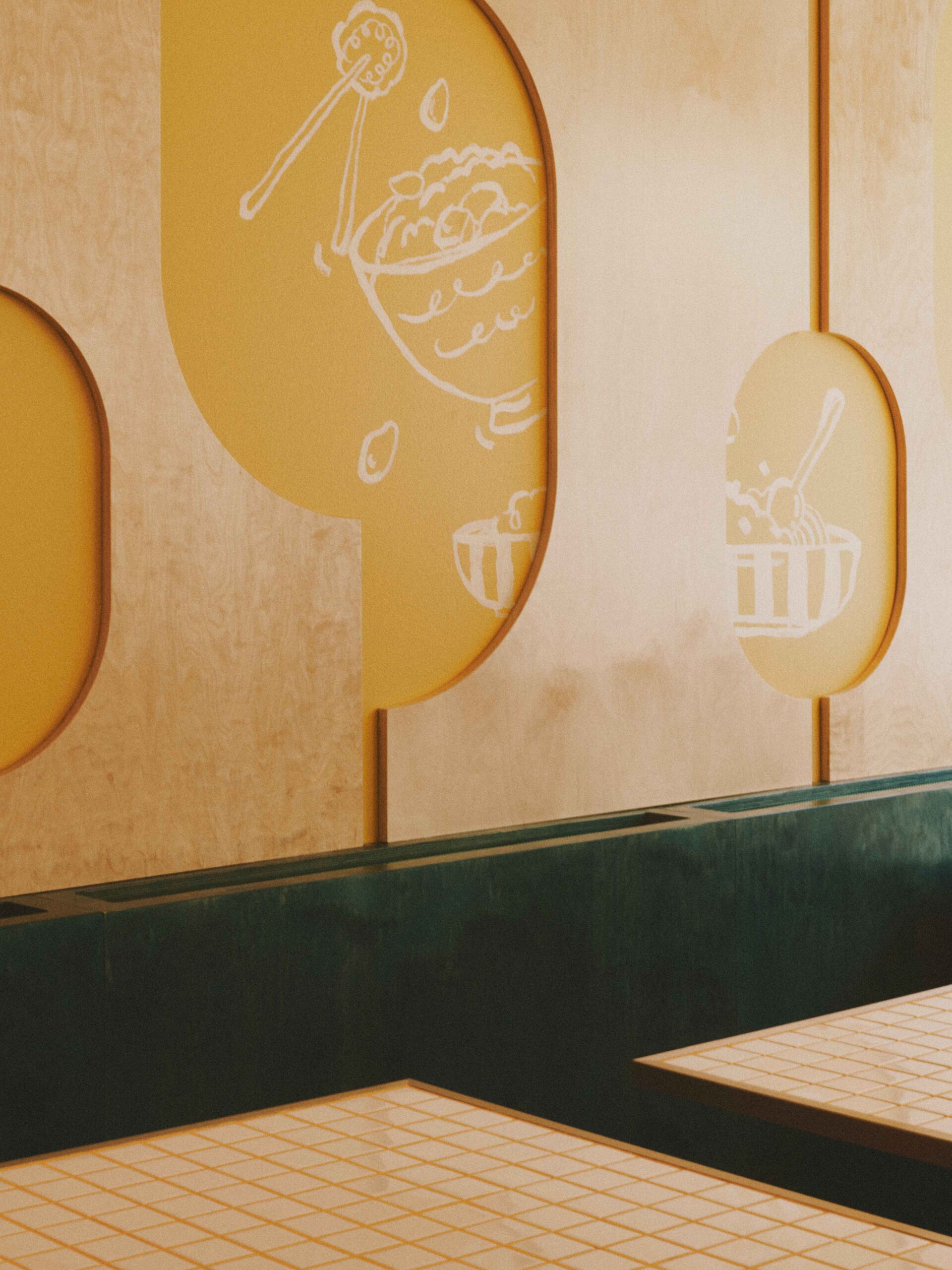 Interior wall with yellow panels featuring white sketches of bowls with food, above dark green booth seating.