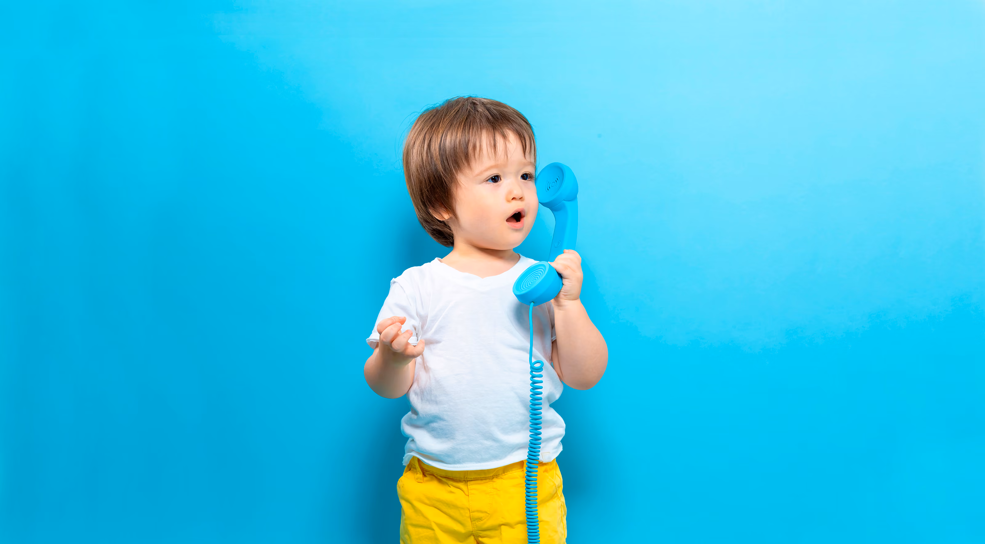 A little boy stands near a blue background and holds a phone in his hands