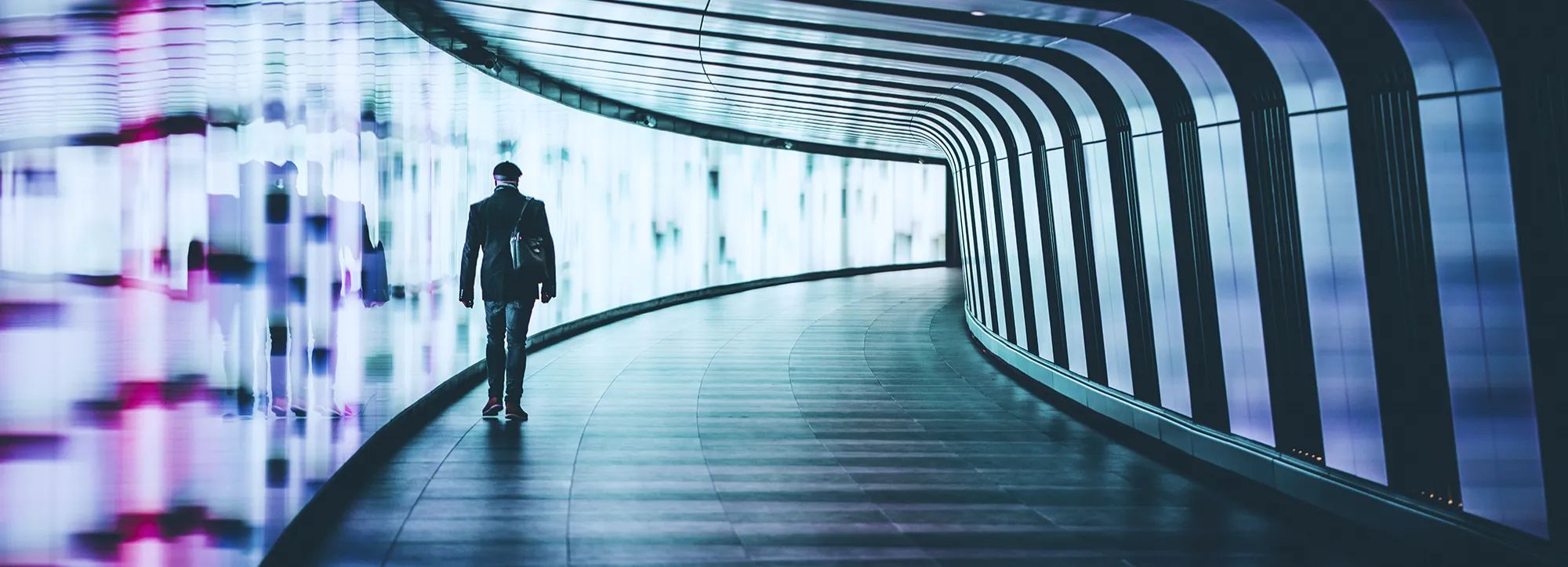 Person walking alone through a futuristic curved walkway with blue and purple lights.