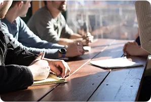 People sitting around a wooden table, taking notes and discussing during a meeting.