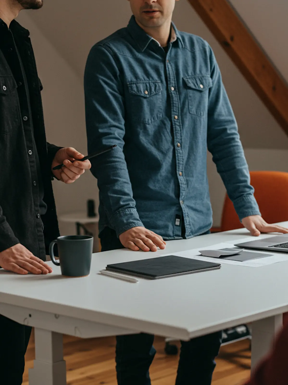 A couple of men standing around a table with a laptop.
