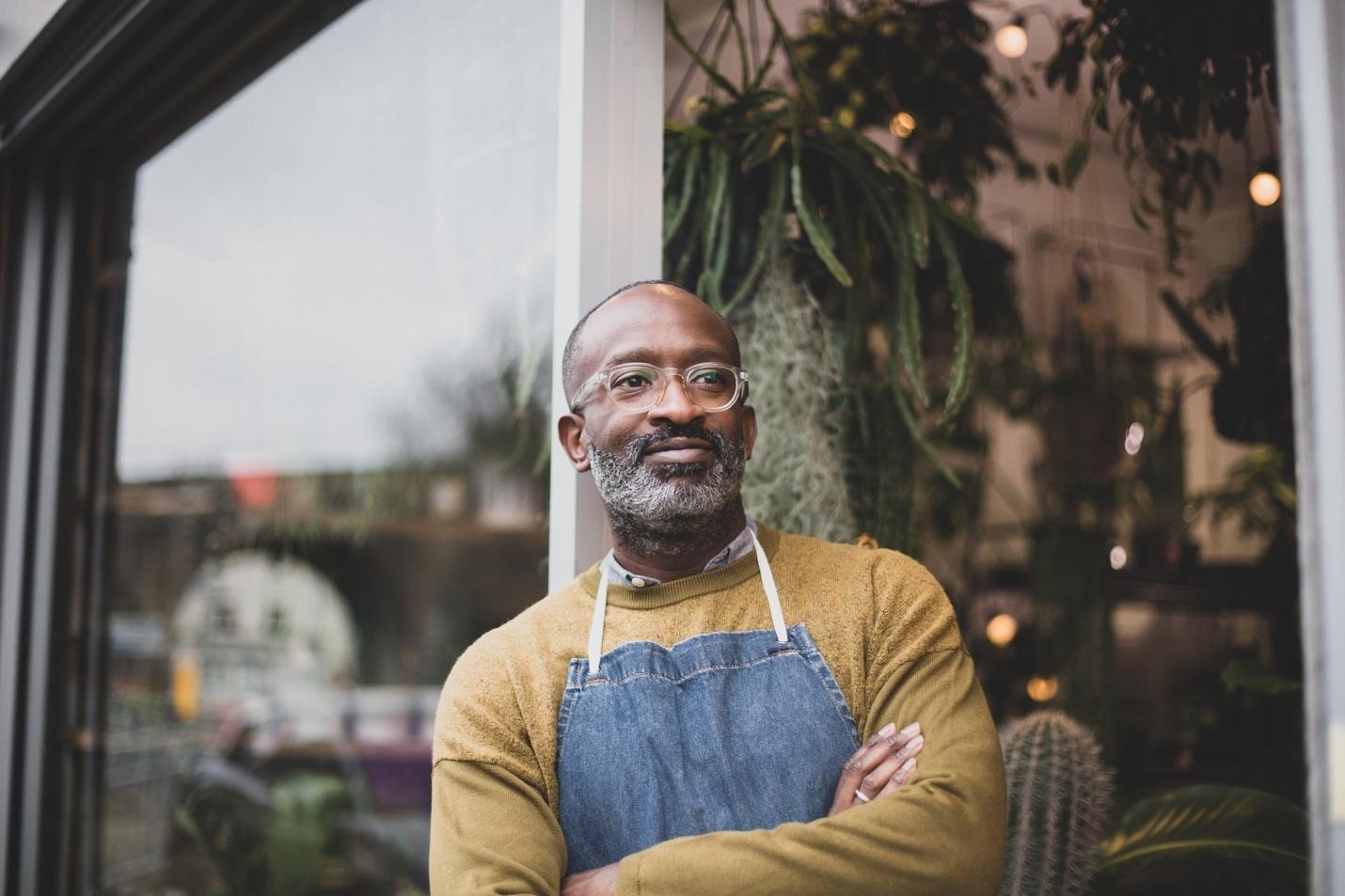 Man in apron leaning against shop entrance