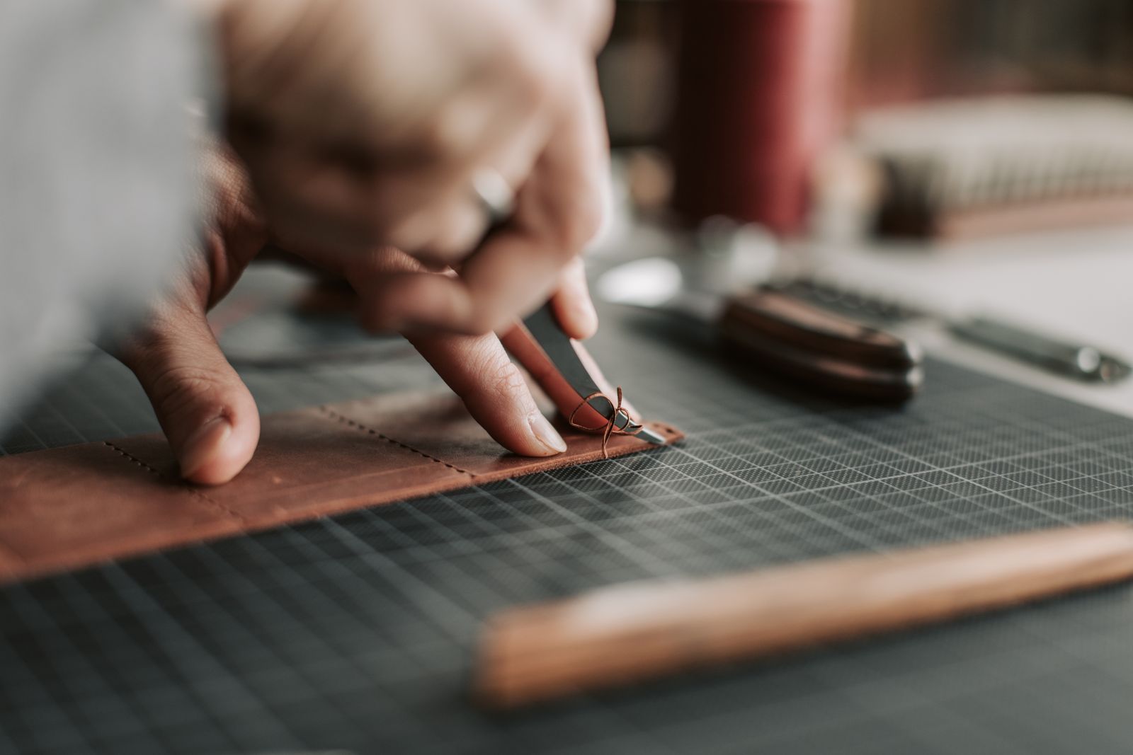 Close-up of a craftsperson's hands cutting leather on a workbench
