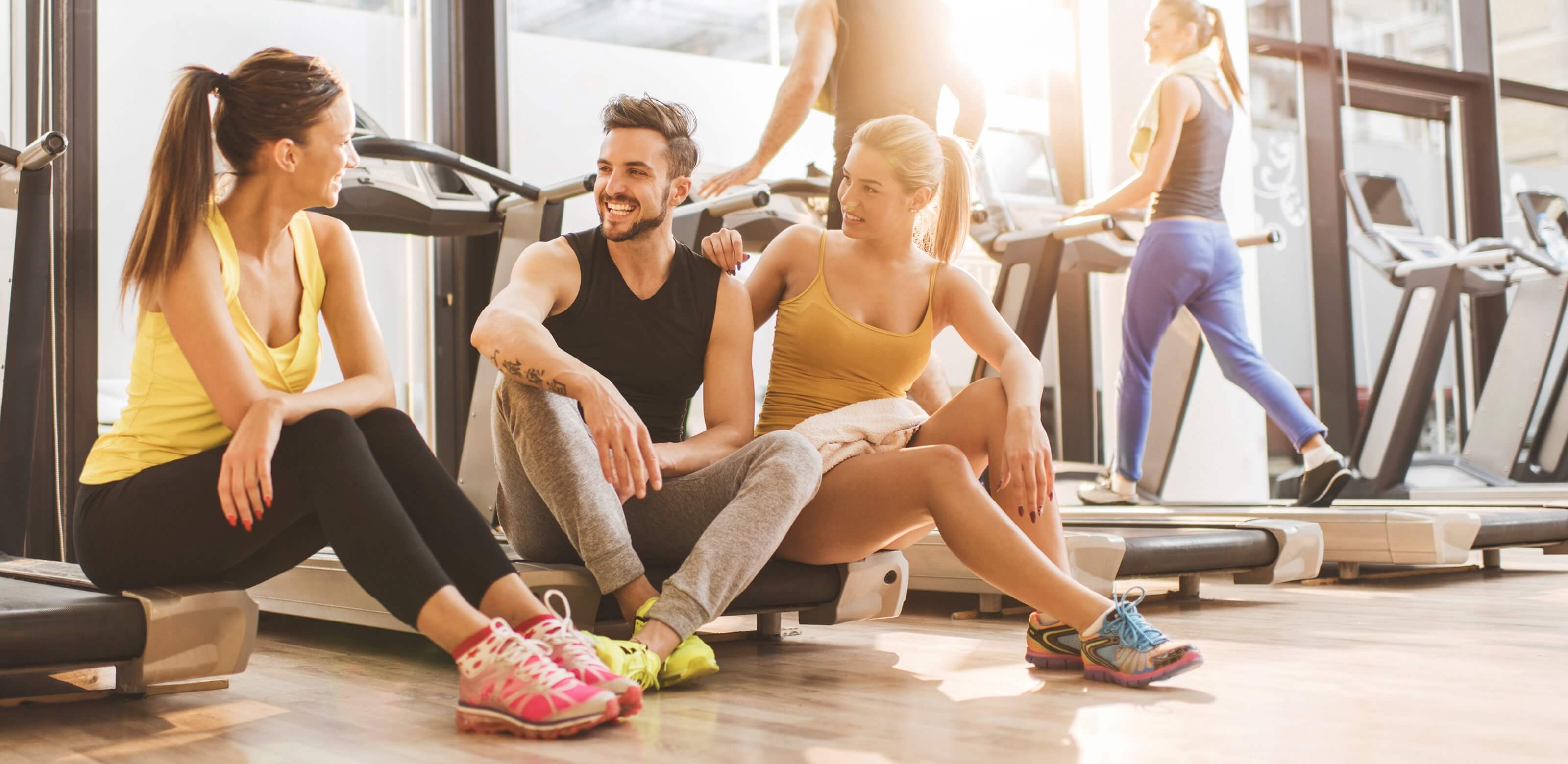 Mehrere Freunde trainieren zusammen im Fitnessstudio und machen bei den Laufbändern eine Pause.