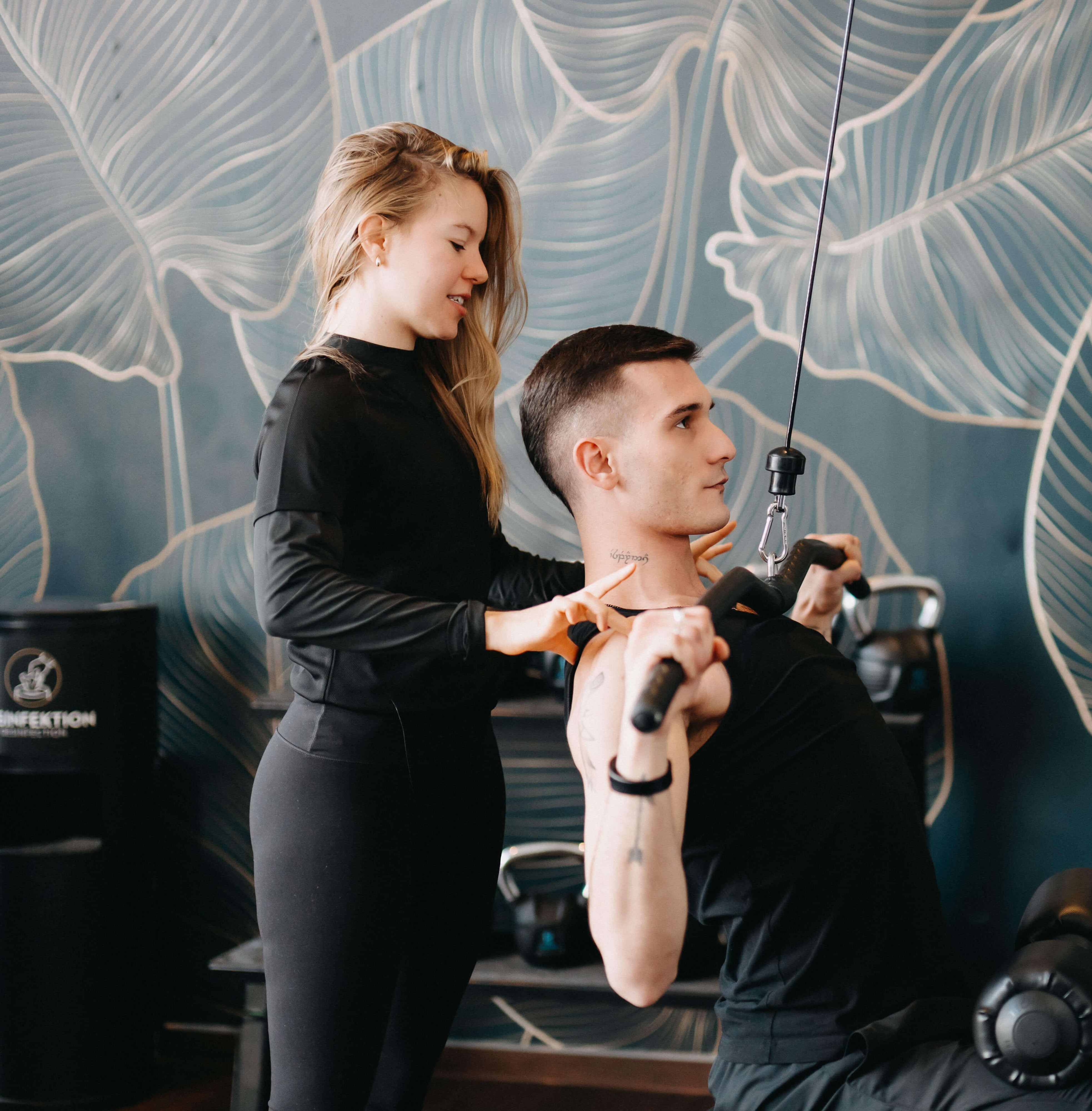 Eine Frau unterstützt einen Mann beim Training am Lat-Zug.
