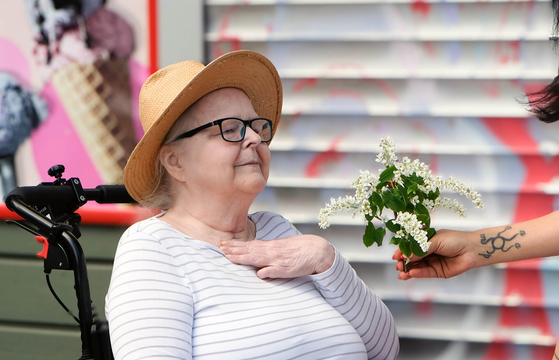 En rullstolsburen kvinna med randig tröja och hatt får en bukett blommor.