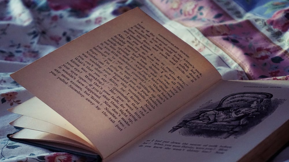 An open antique book sitting on a blanket.