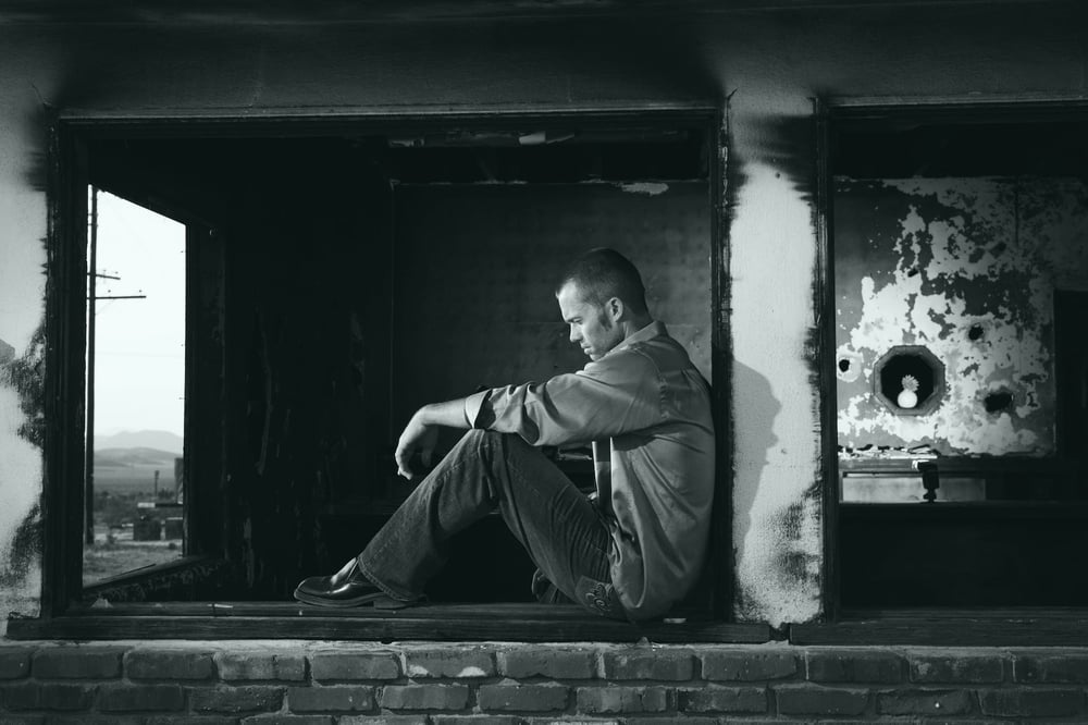 A sad person sitting in the window of a rundown building.