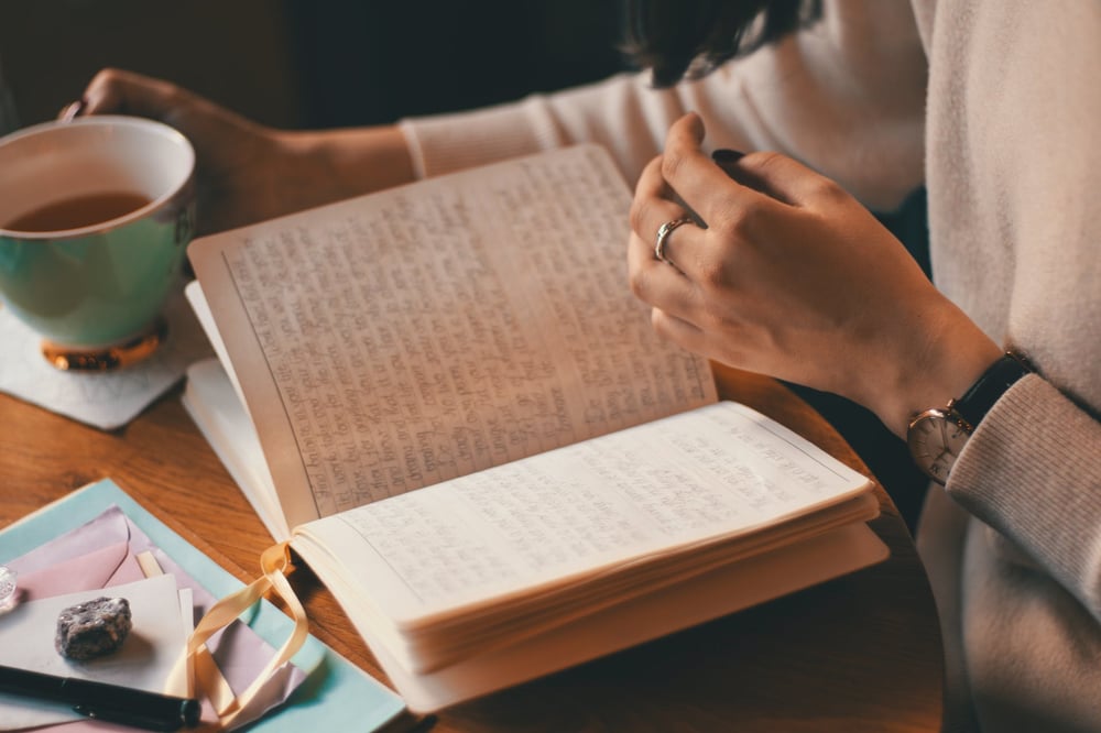 The hands of a person holding a cup of coffee and flipping through the pages of a filled-in journal.