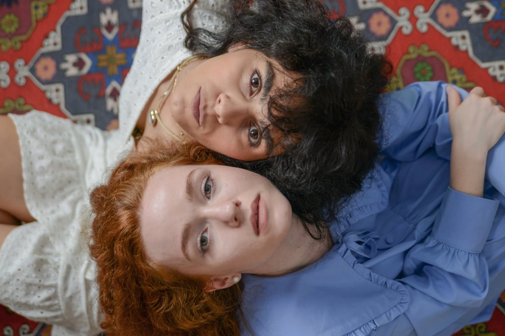 Two people sit back-to-back with their heads tilted upward to look at the camera.