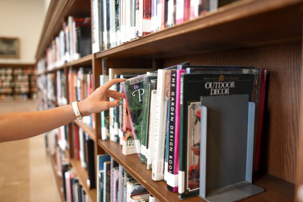 A hand pulling a book off of a library shelf.