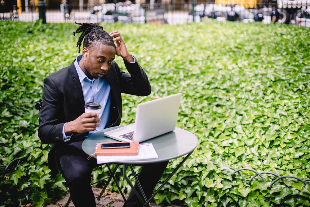 A writer scratches their head while looking at a laptop.