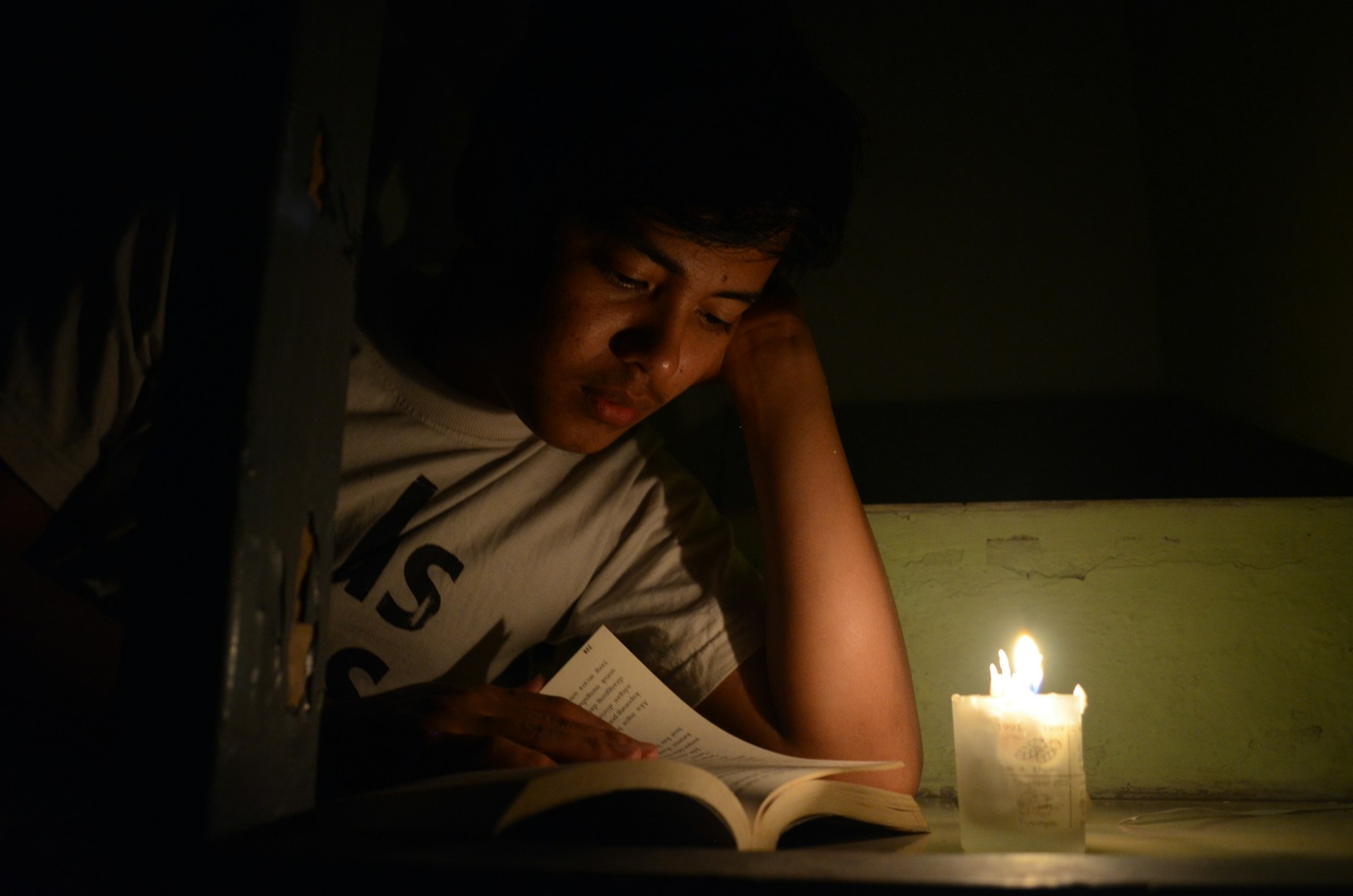 A young person reads a book by candlelight.
