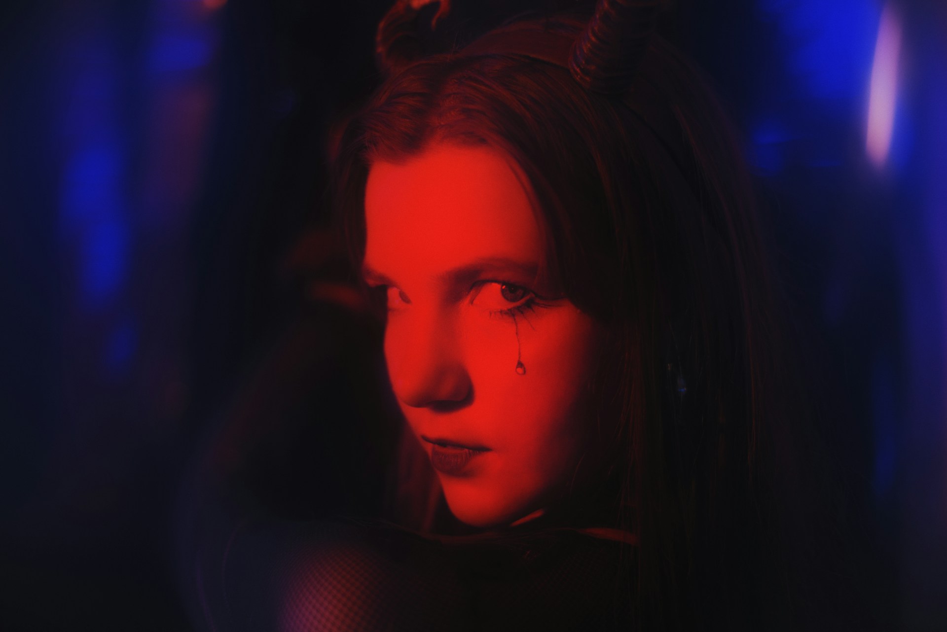A person casts the viewer a sinister look, their face illuminated in red light.