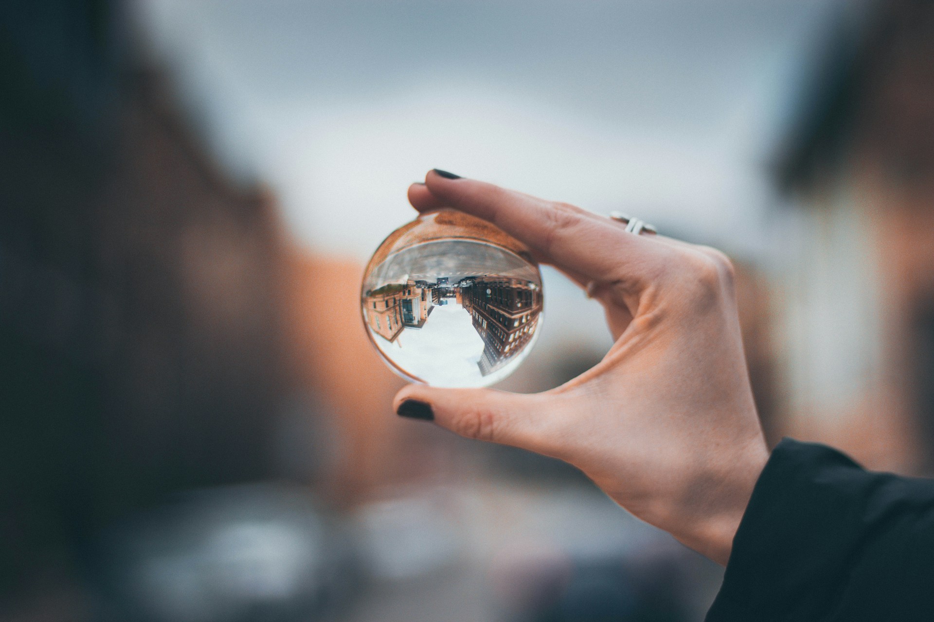 A hand holds up a glass ball that shows an image of a city block turned upside down.