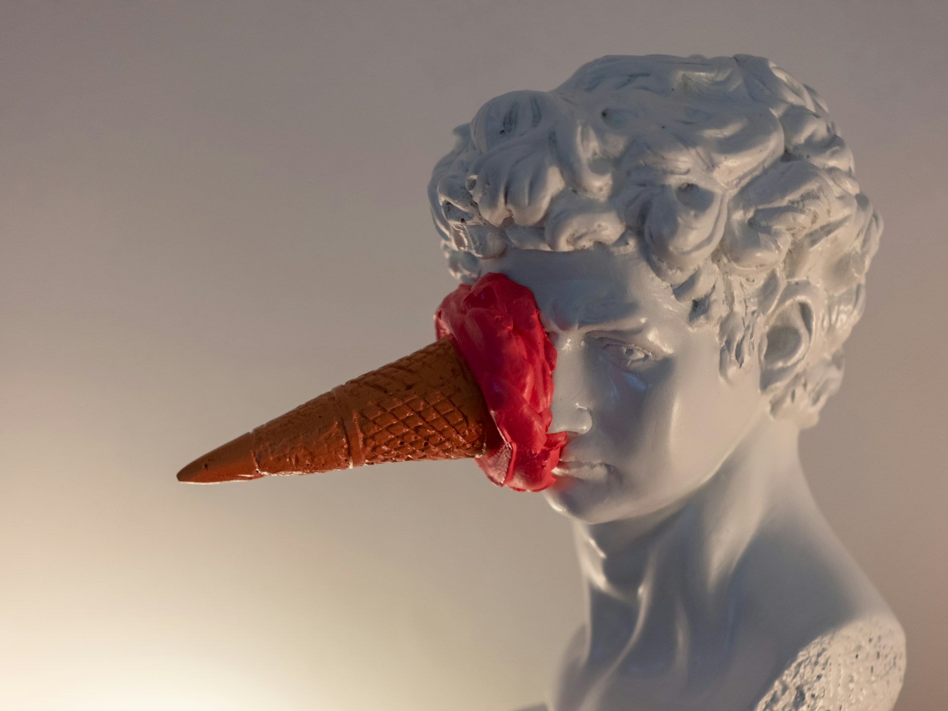 A classical bust of a young man with an ice cream cone smashed into his eye.