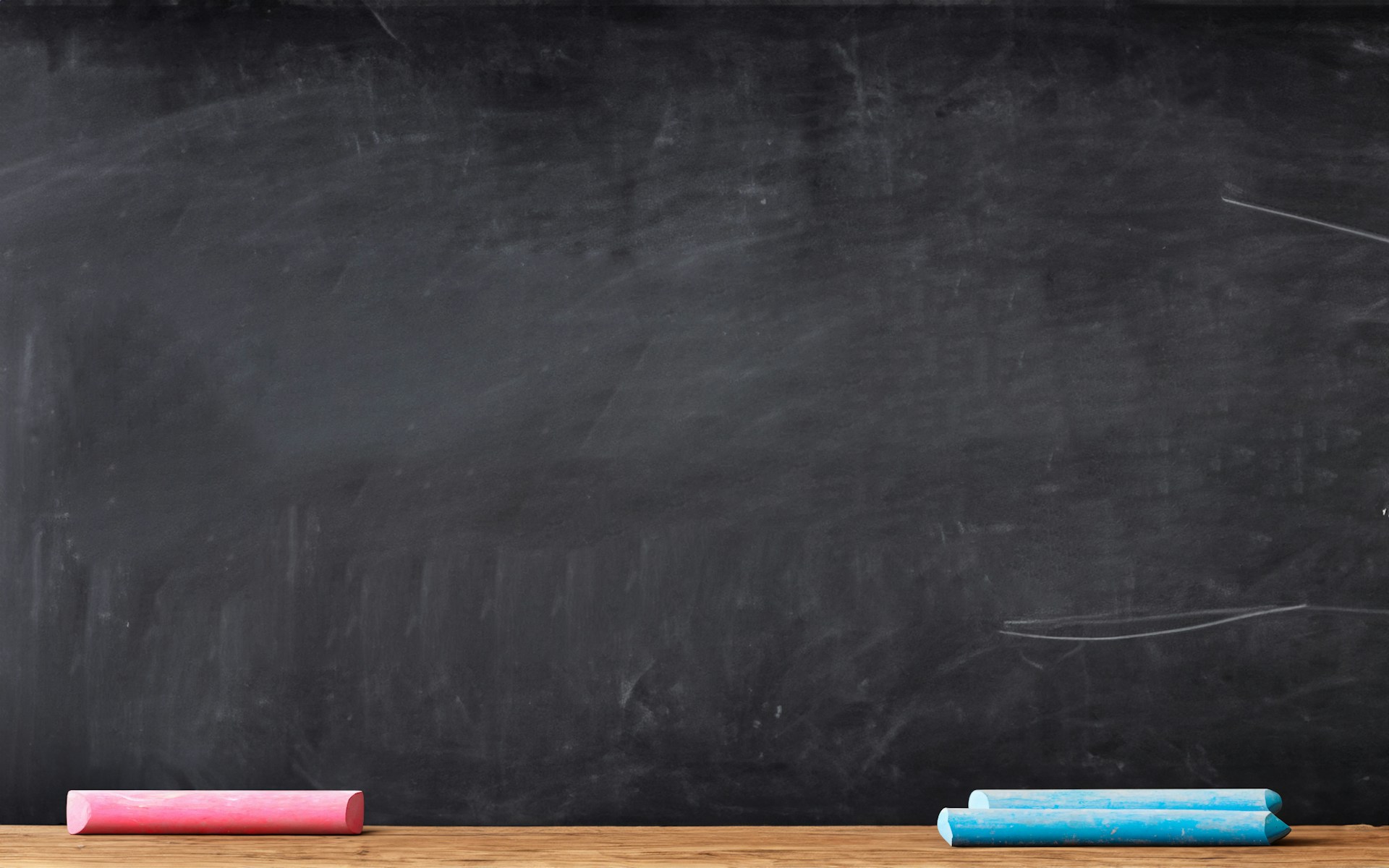 A blank blackboard with pink and blue chalk on the shelf.