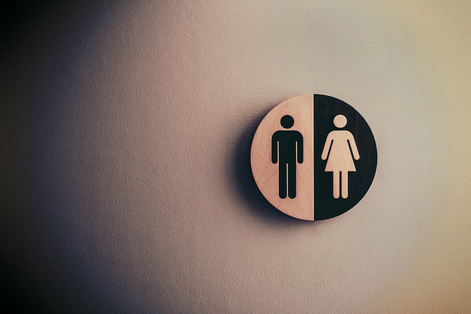 A round restroom sign with one half depicting a male figure and the other half showing a female figure.