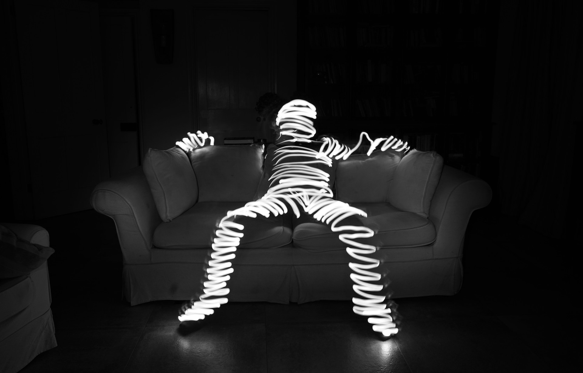 A person made of squiggly light lounges on a sofa.
