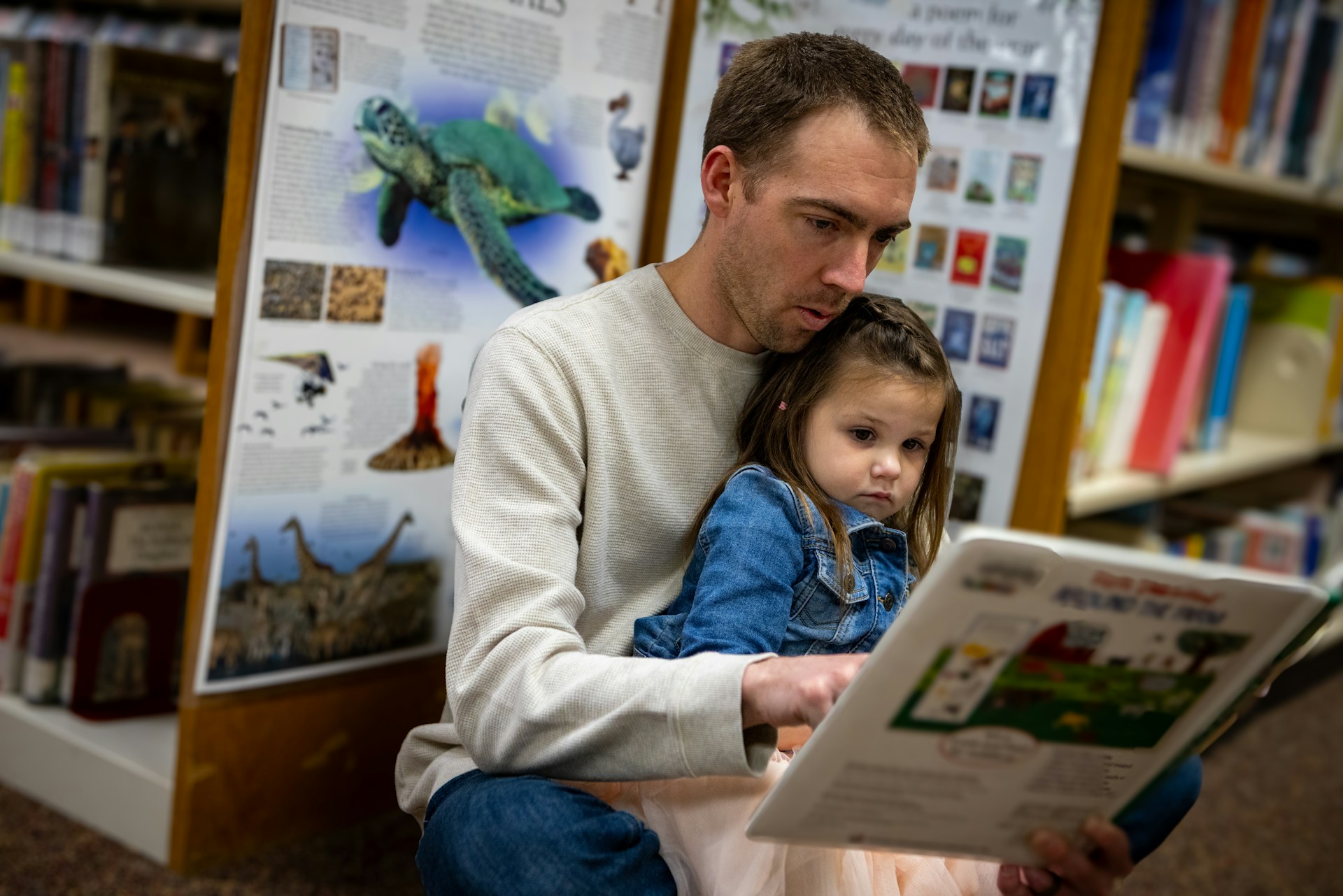 A man points to a page in a children's book as he reads to a child on his lap.e