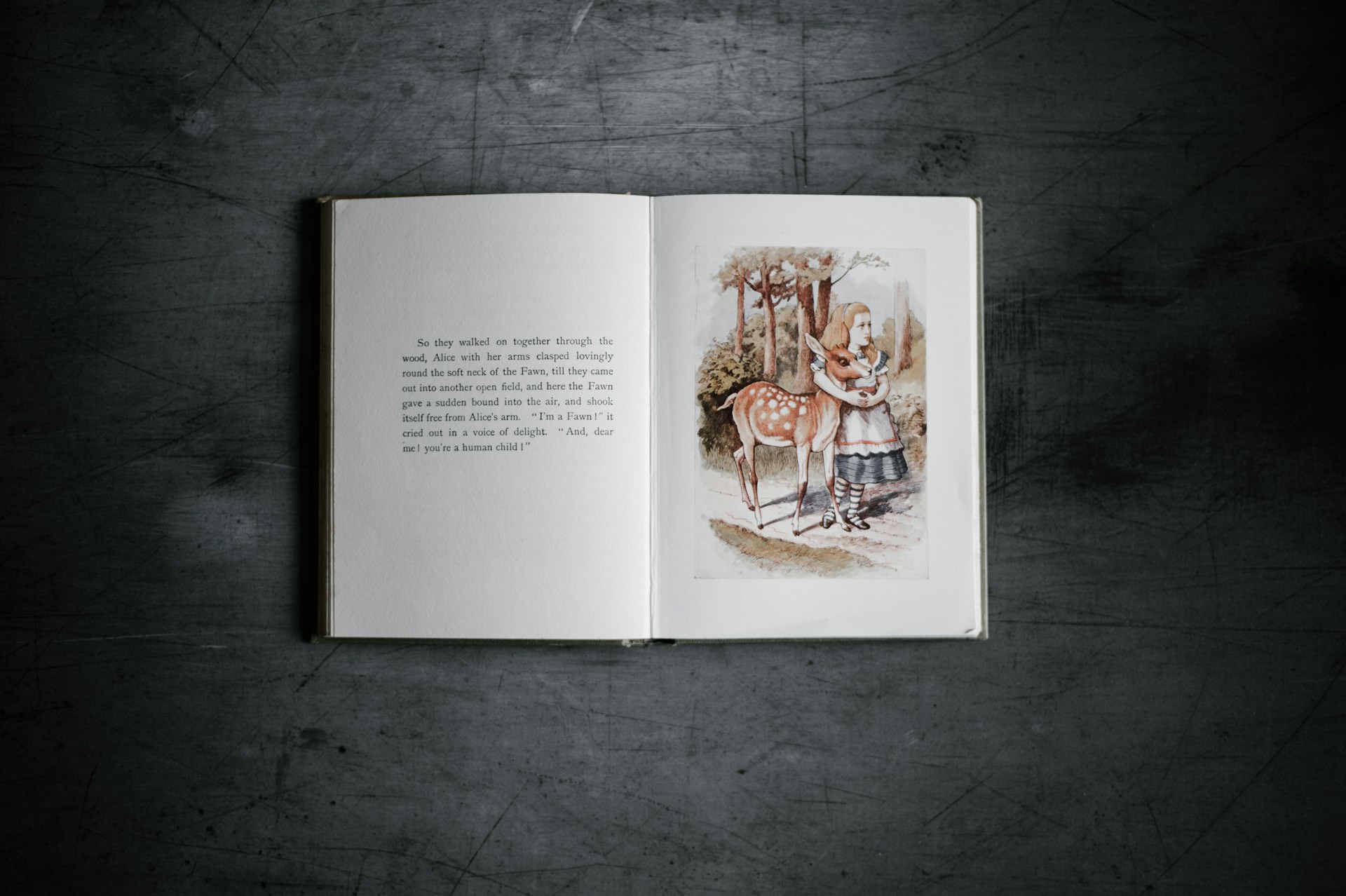 An illustrated copy of Alice's Adventures in Wonderland lies open on a black surface.