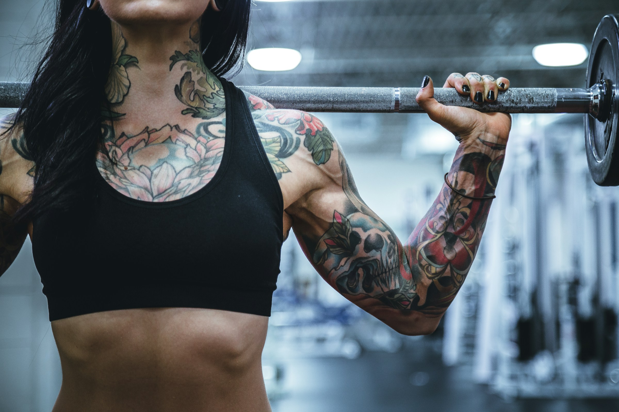 A tattooed person holds up a barbell.