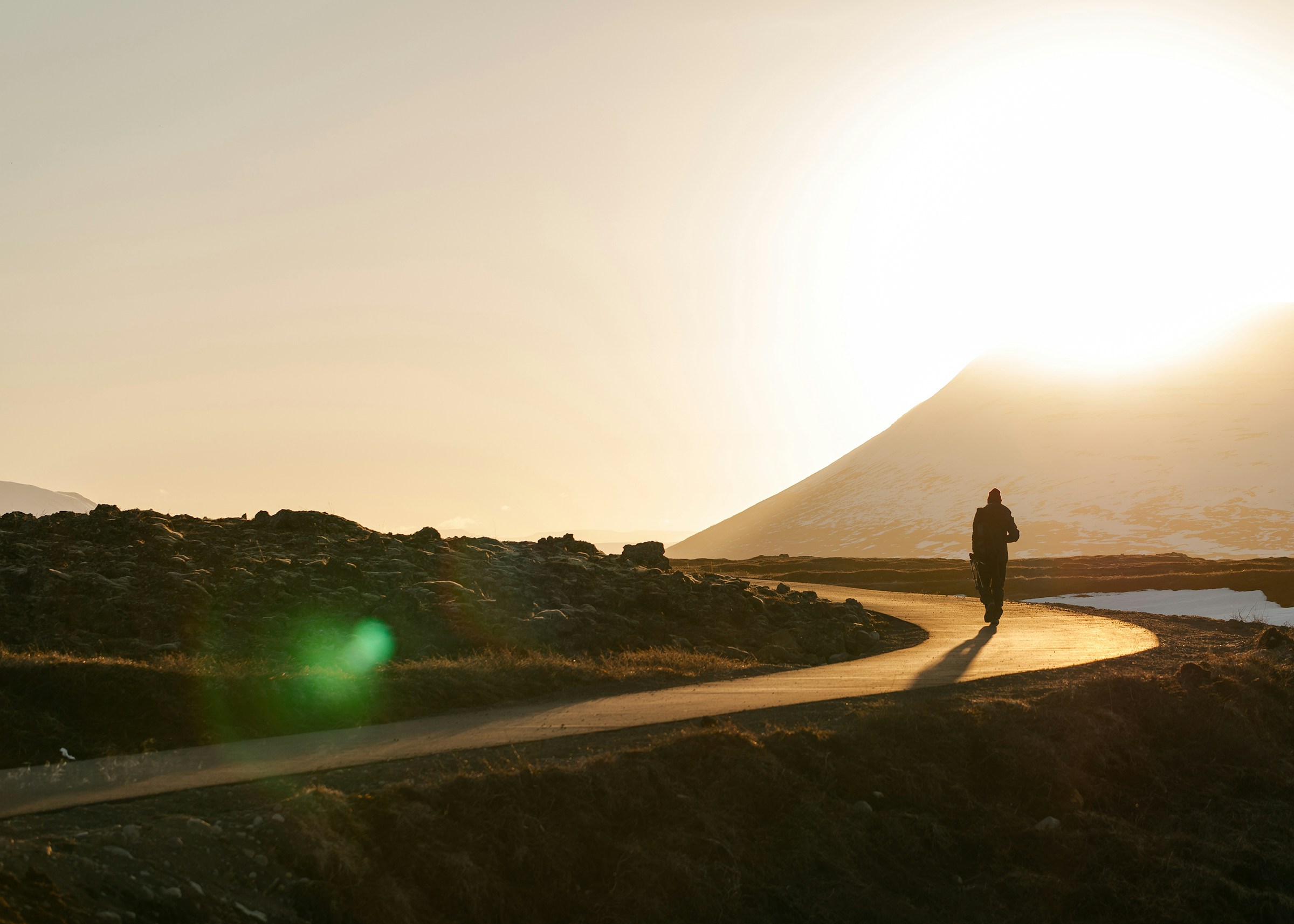 A person walks on an empty road in Iceland at sunset.