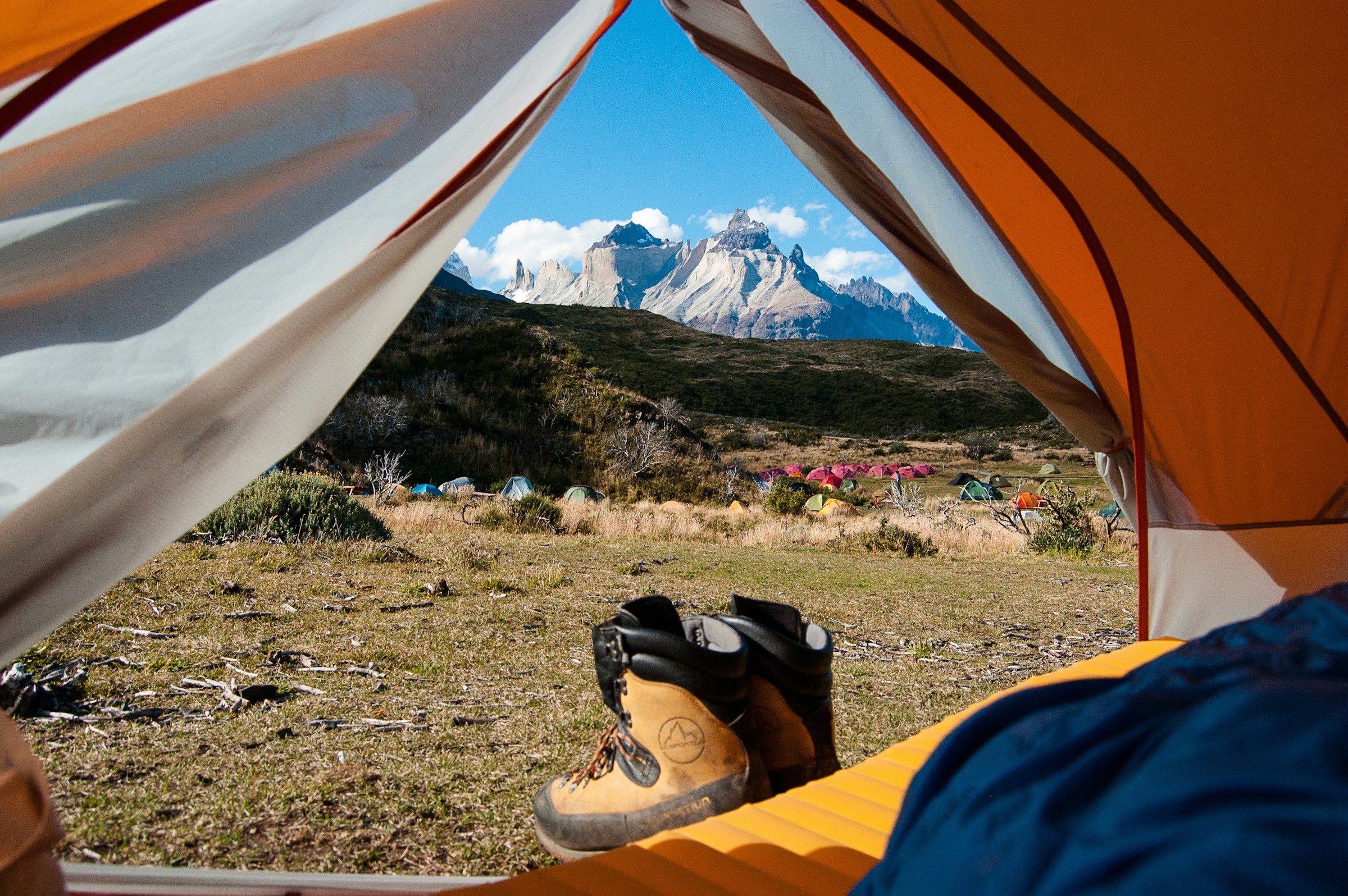 A view of beautiful mountains through the open flap of an orange tent.