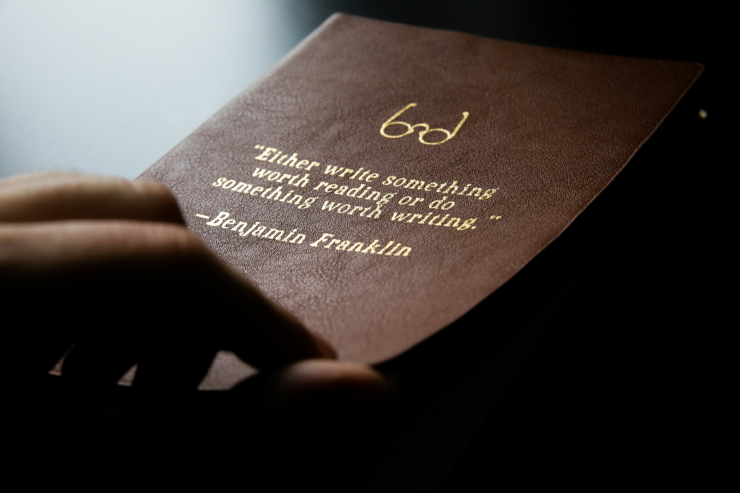 A brown leather journal with gold words reading, "Either write something worth reading or do something worth writing." –Benjamin Franklin
