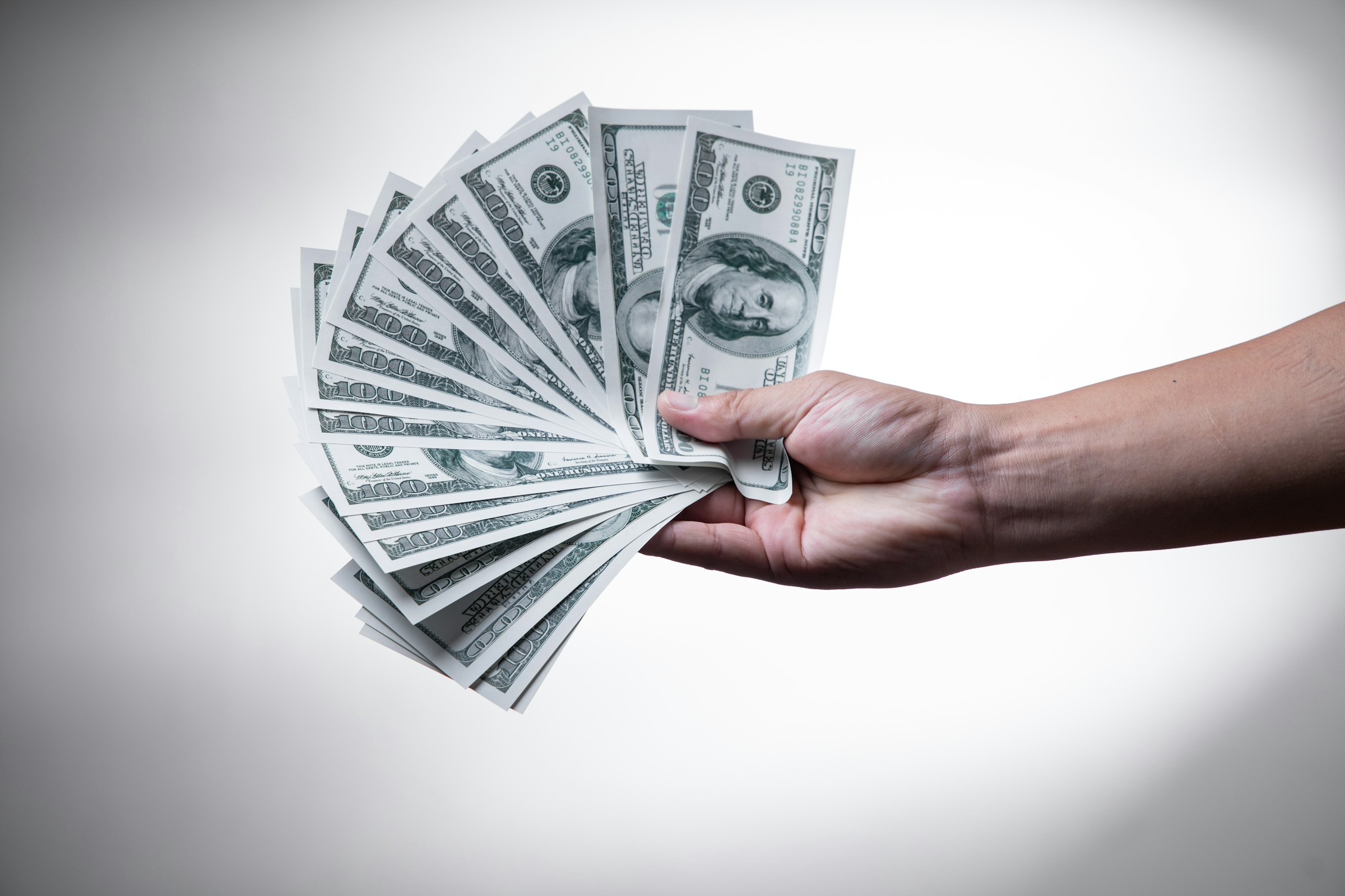 A hand holds several $100 bills fanned out.