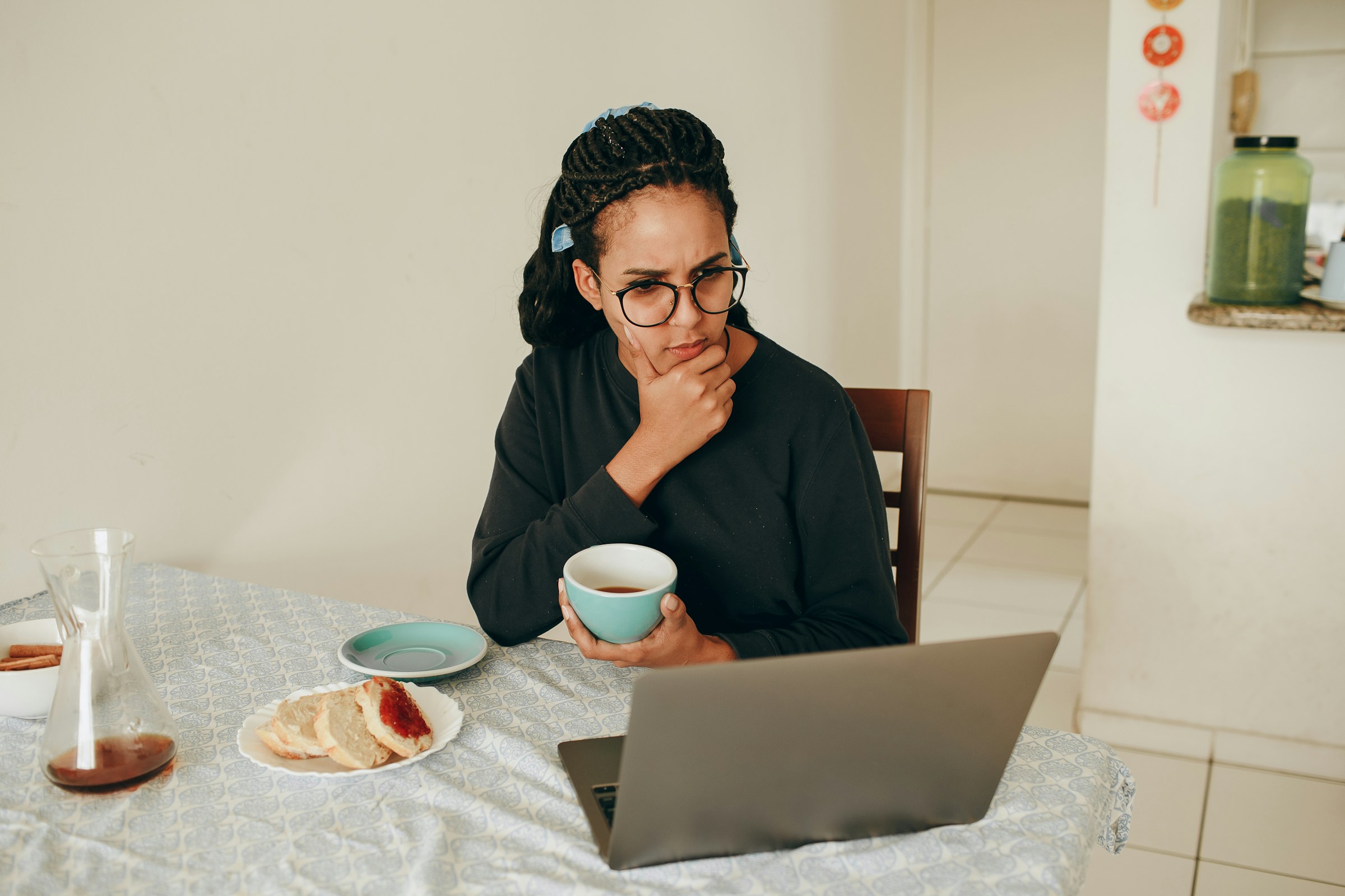 A person sits at a computer holding a cup of coffee and thinking.