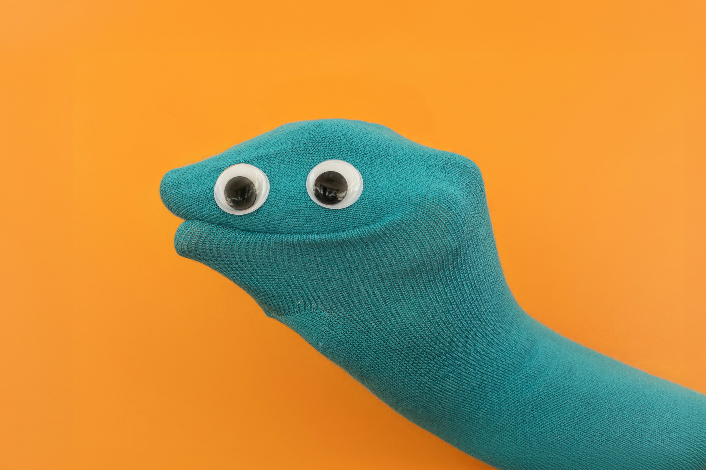A hand inside a turquoise sock puppet with two googly eyes.