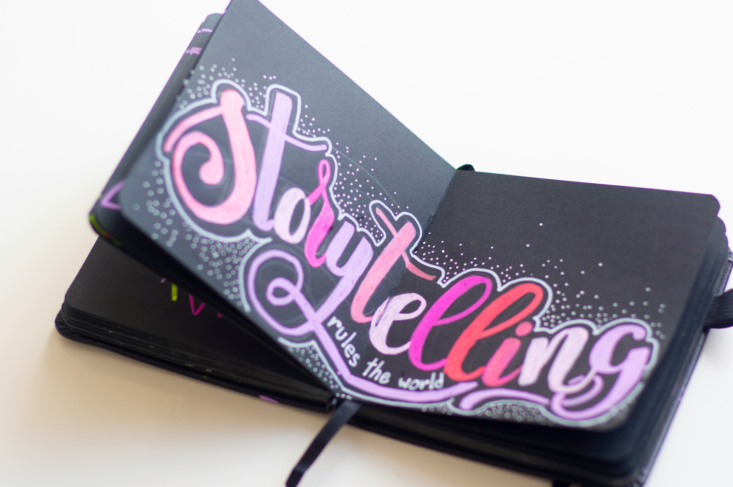 An open black notebook with pink lettering that reads "Storytelling rules the world."