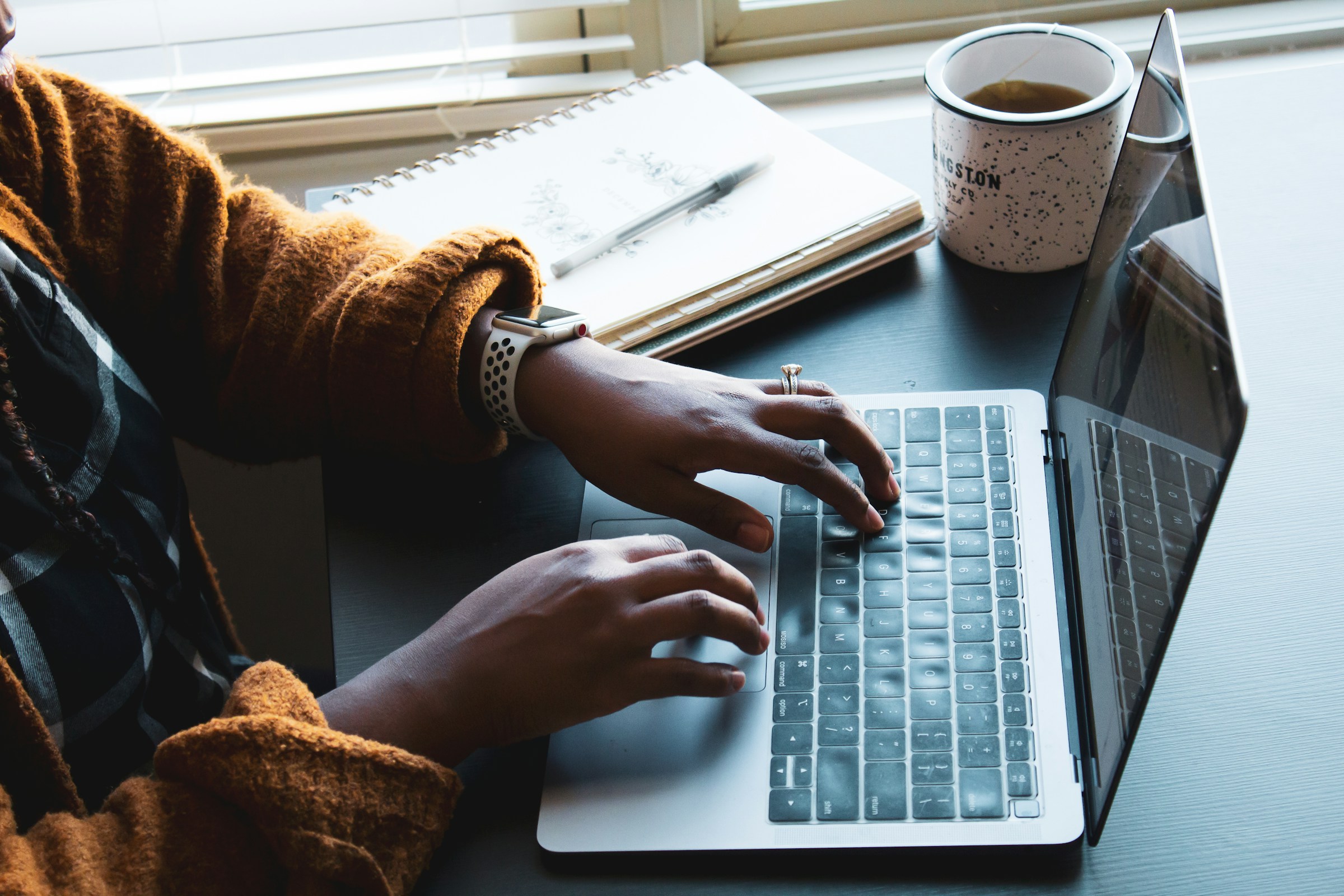 A person in a fuzzy orange sweater types on a laptop.