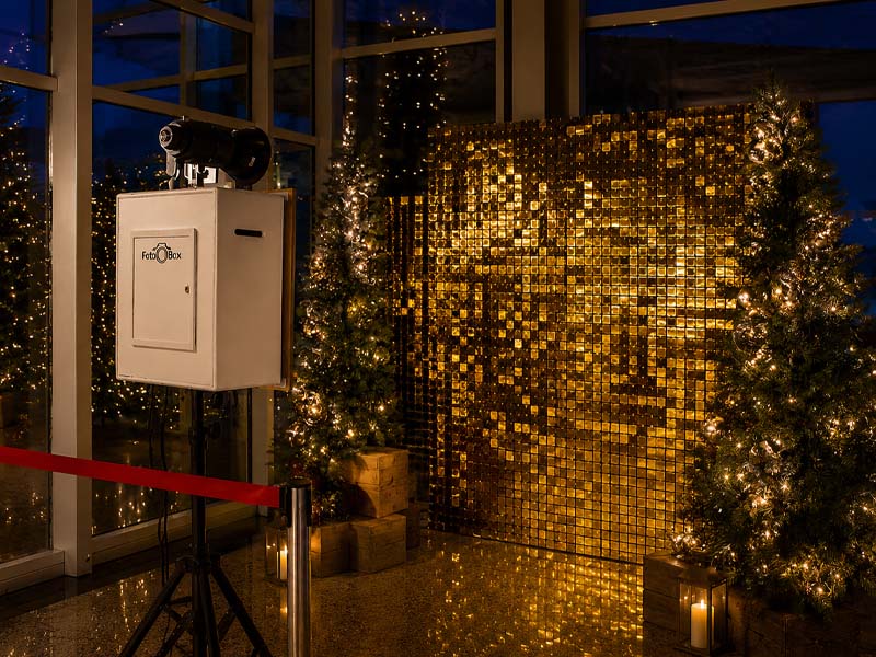 Weihnachtlich beleuchteter Innenbereich mit Fotoautomat, glänzender Goldwand und geschmückten Tannenbäumen.