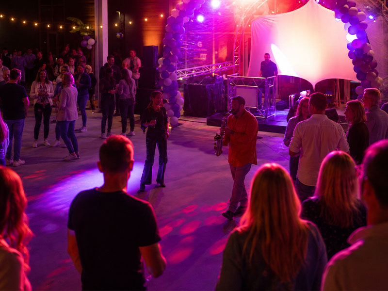 Menschen tanzen und hören einem Saxophon-Spieler auf einer Party mit bunten Lichtern zu.