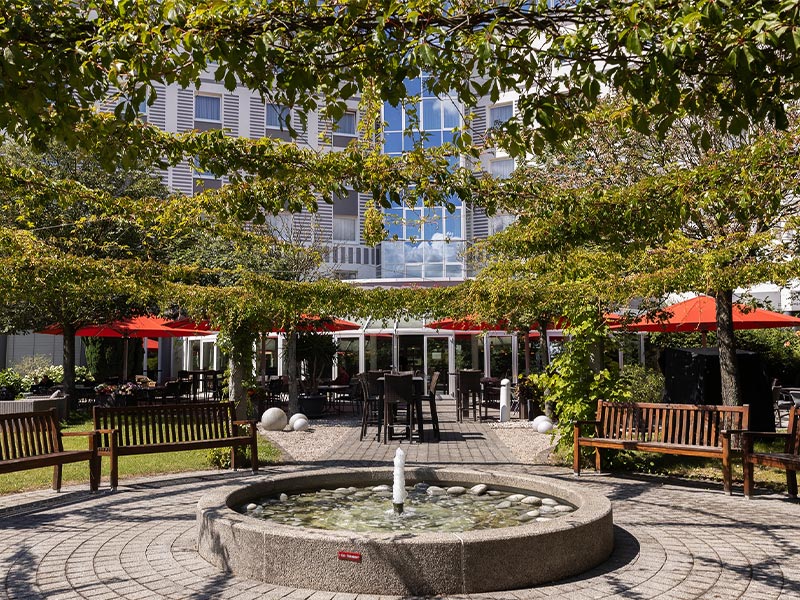 Ein schöner Innenhof mit Springbrunnen, Bänken und Sitzbereich mit roten Sonnenschirmen.