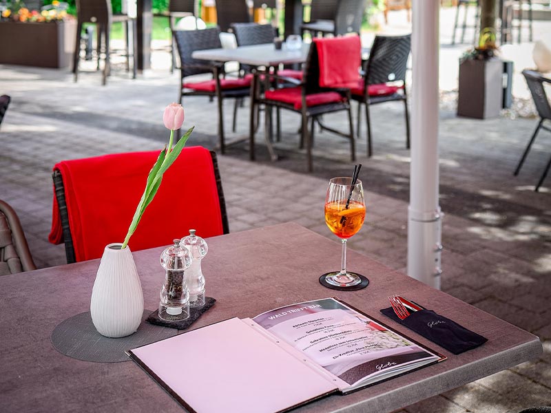 Gedeckter Tisch mit rosa Tulpe, Speisekarte und Getränk in einem Restaurant im Freien.