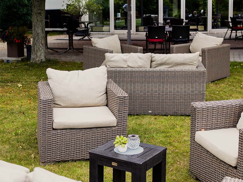 Gartenmöbel aus Rattan mit Kissen um kleinen Tisch auf Gras vor einem Restaurant.